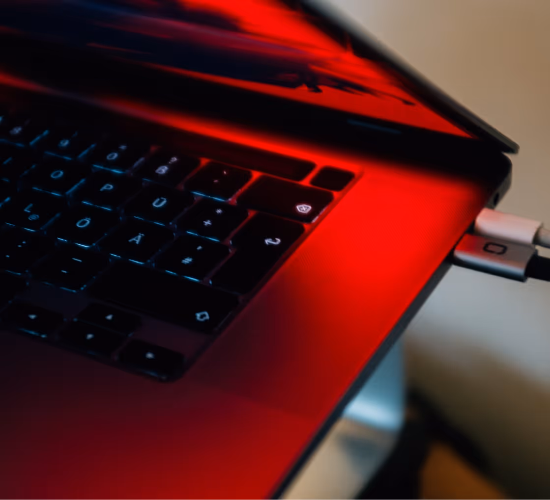 Close-up of a laptop keyboard with two cables connected on the right side and red reflection on surface.